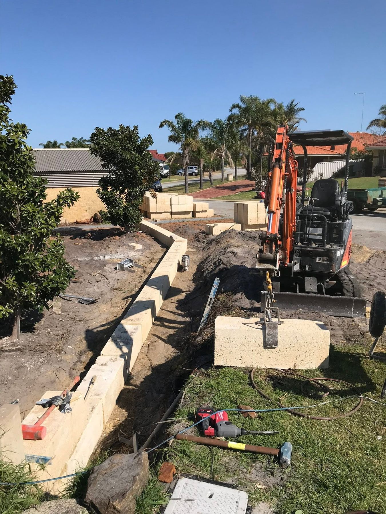 A mini excavator lifting a limestone block into place on a new retaining wall