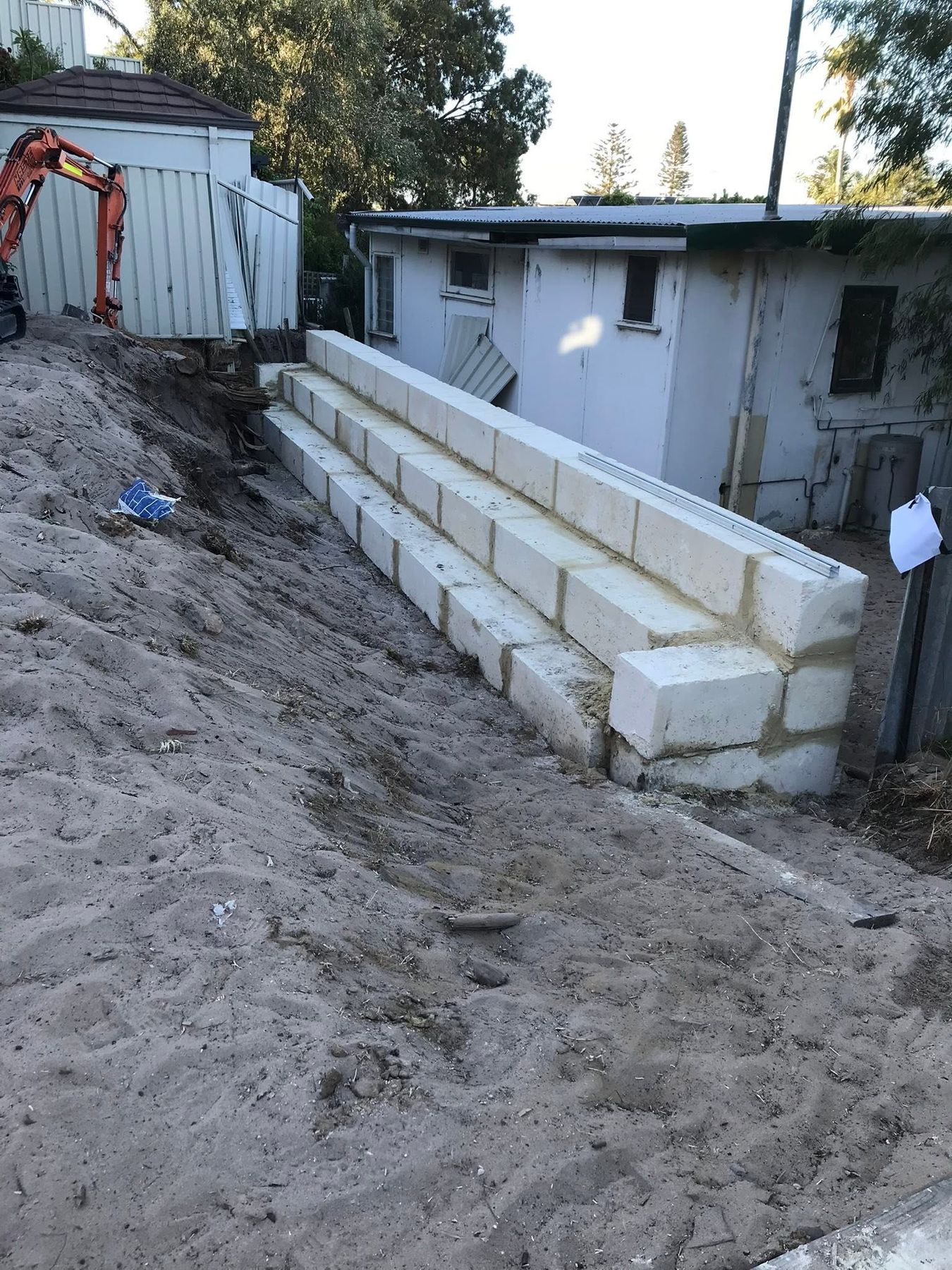A stepped limestone block retaining wall built along a sandy slope