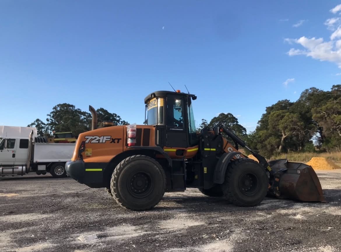 The Haste Contracting CASE 721F XT wheel loader in the yard, bucket down, with a tipper truck behind it