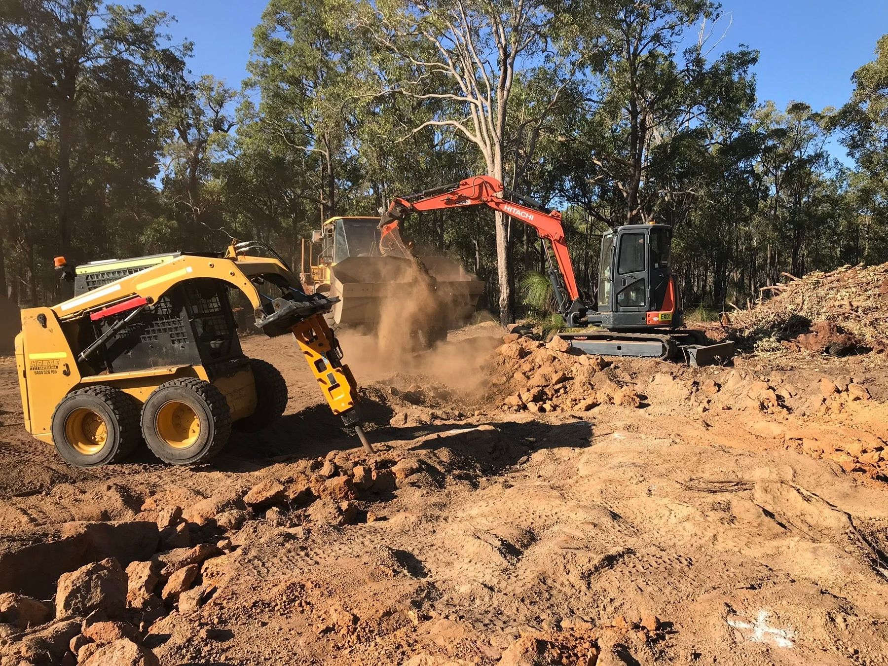 A Haste Contracting skid steer with a rock breaker attachment and an excavator breaking cap rock on a bush block