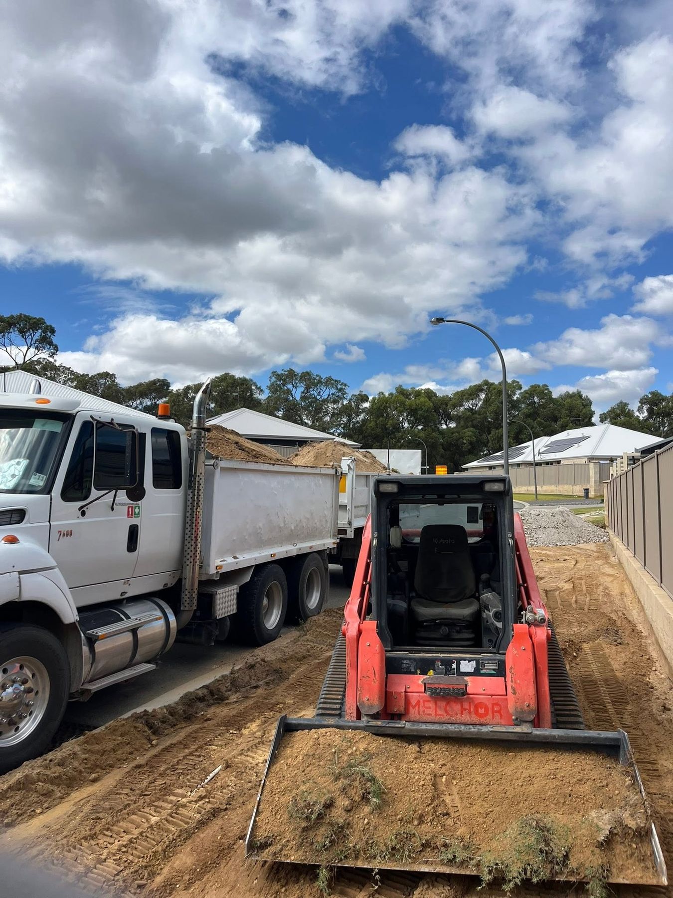 A tip truck loaded with sand beside a tracked loader spreading it on a house block