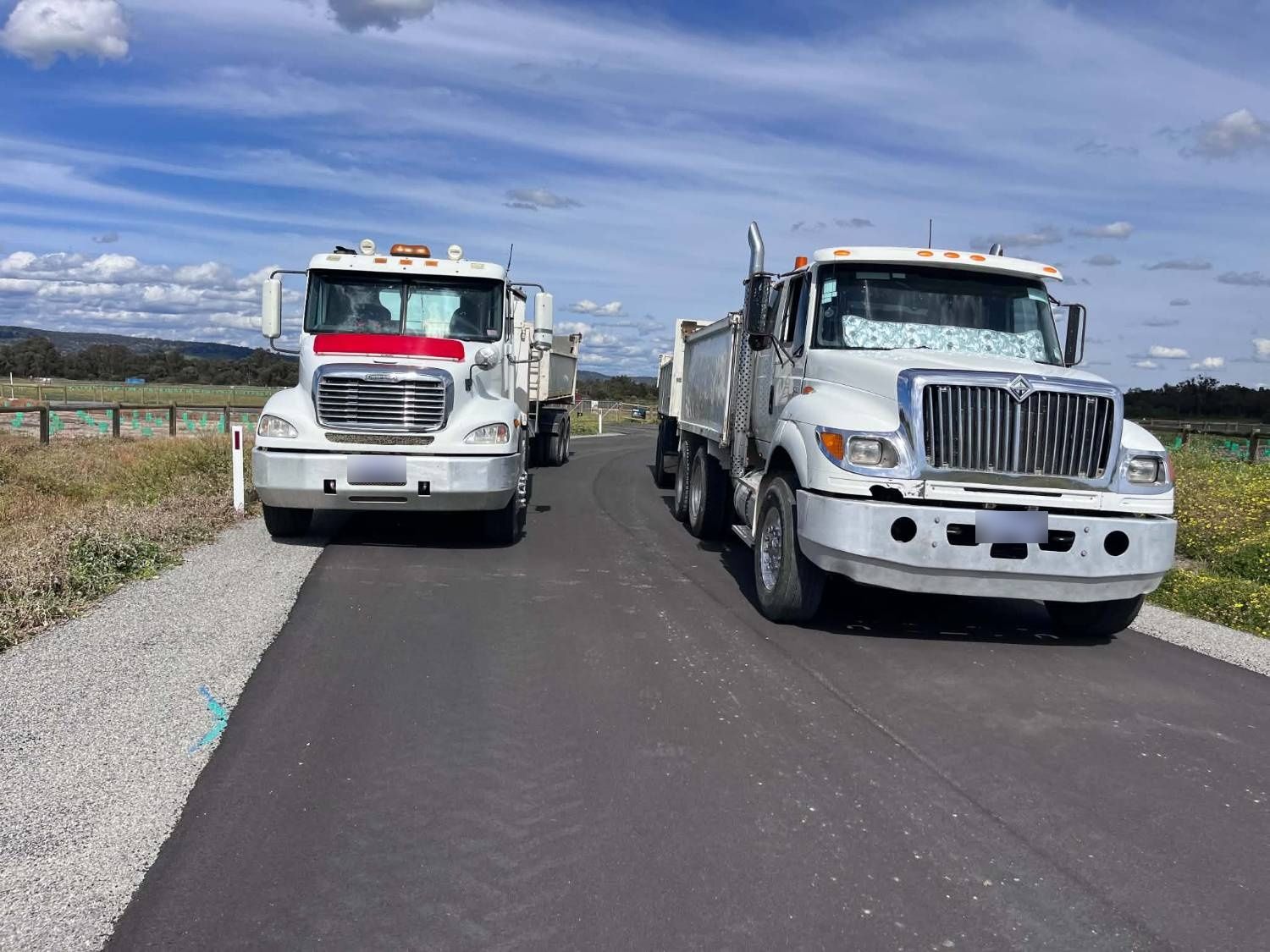 Two Haste Contracting tipper trucks side by side on a freshly laid asphalt road